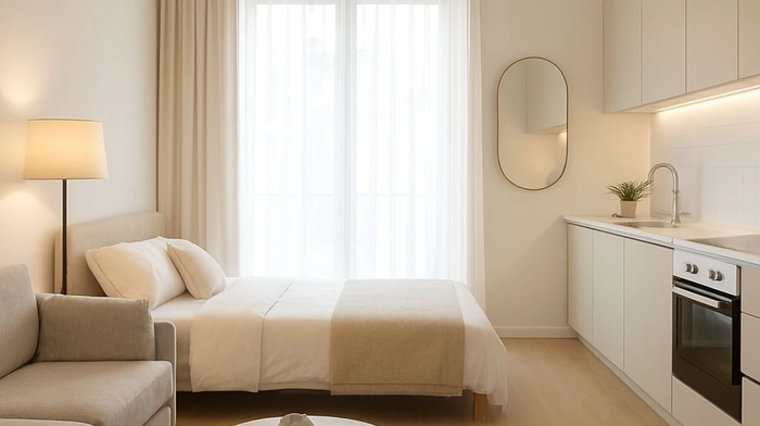 Apartaestudio luminoso con cama, sofá y cocina integrada en tonos claros y diseño funcional
